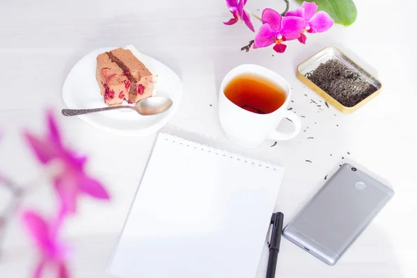 Cup of tea, flowers, spiral notepad, pen. Time management, new day planning concept.