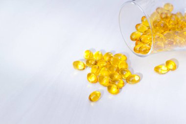 D vitamini içeren sarı kapsüller, beyaz ahşap zemin üzerinde güneş ışığı olan balık yağı omega 3. Sağlıklı ve tıbbi konsept.