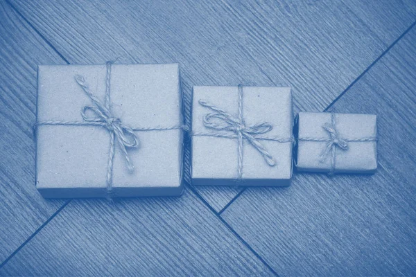 Present wrapped in craft paper with sack rope on wooden background  toned in trendy color 2020 year classic blue. Smaller or bigger concept.