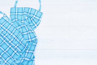 Aşçılık geçmişi, üst görüş konsepti. Beyaz ahşap arka planda mavi ekose piñafore. Boşluğu kopyala.