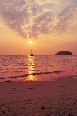 Denizin üzerinde şafak ve küçük bir yelkenli.