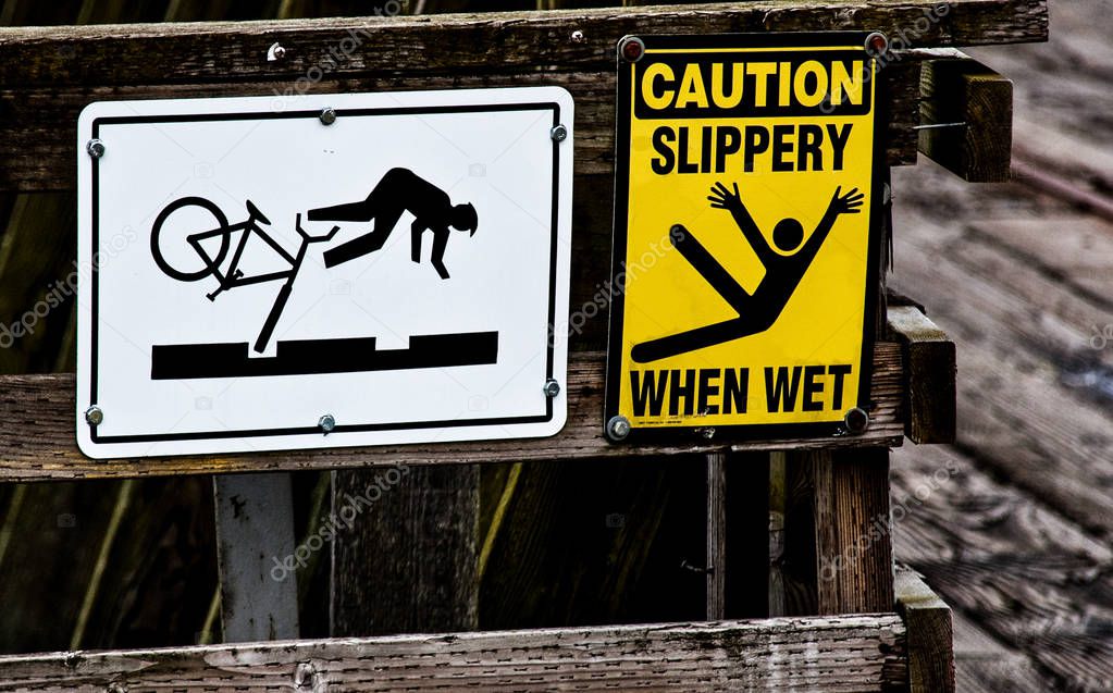 Bicycle and slip & fall danger signs on a wooden rail