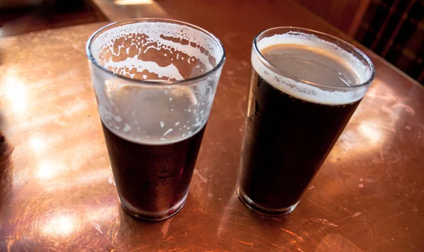 2 große Gläser dunkles Bier auf einem Kupfertisch lizenzfreie Stockfotos