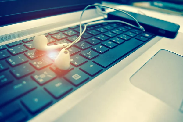 People listen to music on the Internet using a white headset for entertainment.People are shopping online through the Internet,white headphone is placed on the computer keyboard