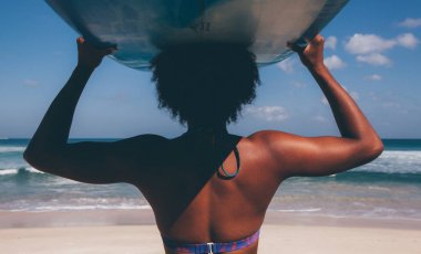 Pasifik Adalı melanesian Papua sörfçü kız mavi longboard Padang Padang Beach, Bali, Endonezya kumda yürürken kafasına taşıyan afro saç modeli ile