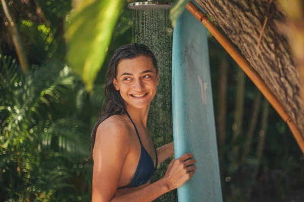 冲孩洗蓝色冲浪板在户外淋浴与热带植物在巴厘岛冲浪营 印度尼西亚 — 图库照片