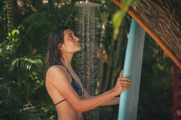 冲孩洗蓝色冲浪板在户外淋浴与热带植物在巴厘岛冲浪营 印度尼西亚 — 图库照片
