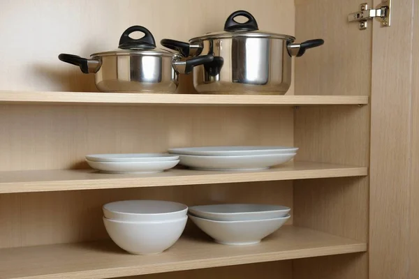 Different white dishes and pans in cupboard in the kitchen.Scandinavian style.Concept order in the cupboard in the kitchen.