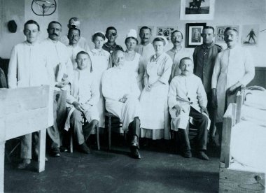 wounded german soldier posing with doctor and red-cross sisters in hospital room clipart