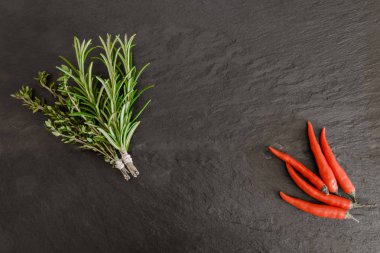 Kekik, biberiye demetleri ve siyah taş yüzey zemin üzerine pul biber