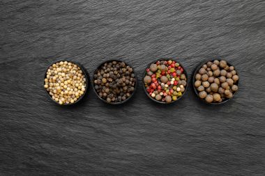 Siyah, yeşil, pembe, beyaz ve güzel kokulu biber taneleri yuvarlak kavanoz siyah taş yüzey arka plan üzerine yerleştirilen