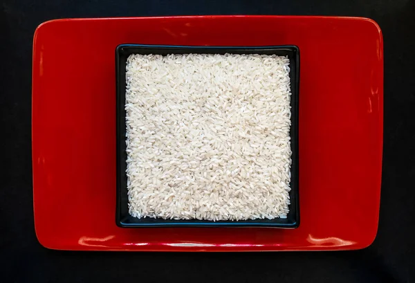 Зерна риса в черной пластине на фоне красной плиты — стоковое фото