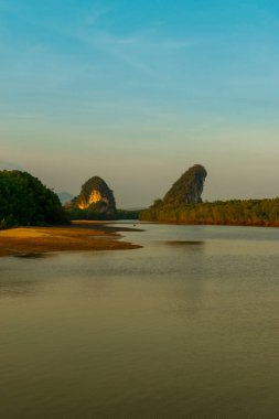 Khao Khanab Nam dağlarının manzarası ve Tayland 'ın Krabi kasabasındaki alçak gelgitler sırasında nehir kanalı ve sarı günbatımı ve mavi gökyüzü ile aydınlatılıyor.