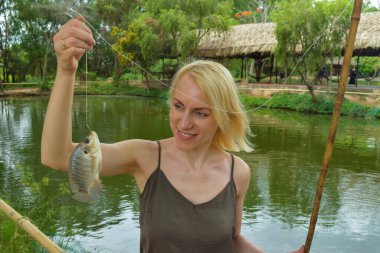 Genç sarışın kadın Vietnam 'daki su birikintisinde bambu yolu ile yakalanan tropikal balıkları gösteriyor.