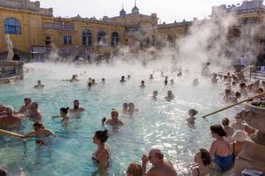 Budapeşte, Macaristan - 02/19/2018: termal hamam Szchenyi rahatlatıcı ile açık hava güneşli günde insanlar. Ünlü Macar spa Hamam. Sakin ol ve eğlence kavramı. Sıcak termal yüzme havuzu üzerinde buhar.