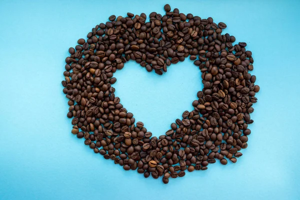 Roasted coffee beans with heart open space in the middle on blue background. Aroma drink concept. Breakfast background. Coffee closeup with copy space. Cappuccino and espresso concept. Love coffee.