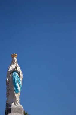09 / 29 / 2019 - Lourdes, Fransa: Beyaz taclı Bakire Meryem 'in güzel heykeli. Beyaz Hanım heykelimiz açık mavi gökyüzü arka planında. Dua ve inanç kavramı. Dini sanat ve mimari. 