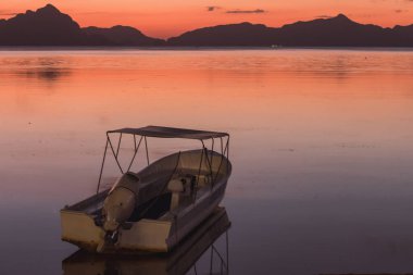 Filipinler 'de güzel sakin bir günbatımı, Palawan. Ufukta adalar ve dağlar olan denizde bir tekne. Denizde akşam karanlığı. İyi akşamlar deniz manzarası. Tropik bir göl. Gün batımının parlak renkleri.