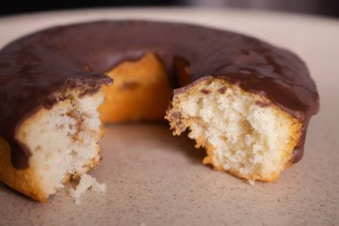 Isırılmış çikolatalı çörek. Ev yapımı çörek tonlu görüntü. Taze fırın. Çikolata kaplı tatlı yuvarlak pasta. Tabakta çikolatalı çörek var. Lezzetli pasta konsepti. Güzel kahvaltı konsepti. 