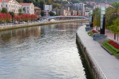 Bilbao manzaralı şehir manzarası. Bilbao 'daki Nervion nehri üzerindeki köprü. Bilbao simgesi, Bask ülkesinin başkenti, İspanya. İspanya 'da renkli bir sonbahar. Nehir kenarındaki güzel gezinti sokağı. Nervion Nehri kıyısında evler ve ağaçlar. 