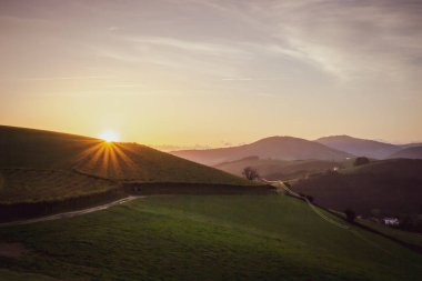 Dağların üzerinden süzülen manzaralı gün doğumu. Sabahları dağ yolu açık. Yeşil tepelerin üzerinde güneş ışınlarıyla güzel bir sabah. İspanya 'da yaz kırsalında. Camino de Santiago manzarası. Sıcak güneş ışığıyla vadide sakin bir sabah.