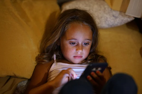 En fyraårig flicka tittar på sin mobil. — Stockfoto