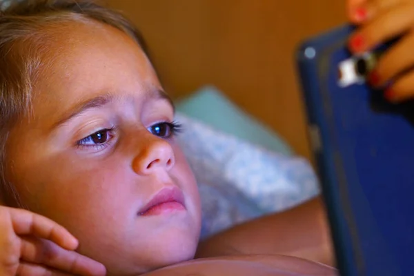 En fyraårig flicka tittar på sin mobil. — Stockfoto
