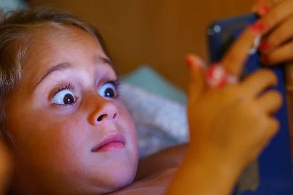 4-årig flicka tittar på sin mobiltelefon med öppna ögon — Stockfoto