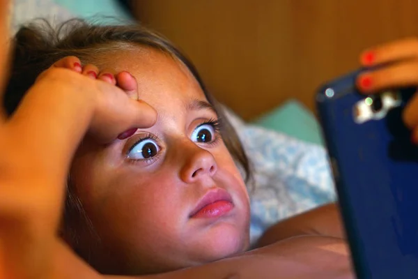 4 살짜리 여자 애가 눈을 크게 뜨고 핸드폰을 쳐다 봅니다 — 스톡 사진