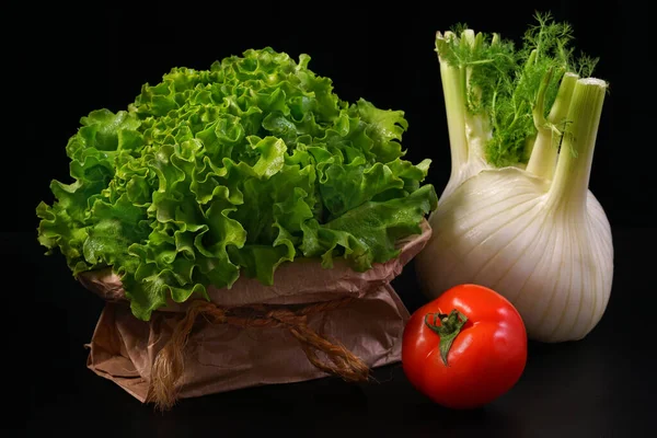 Green lettuce salad with fennel and tomato on black background