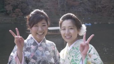 Genç ve güzel Japon kadınları barış işareti nehrin yanında vermek.