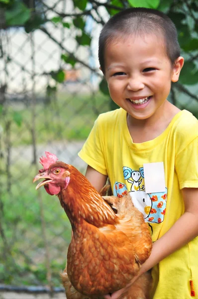 Bir tavuk onun kollarında taşıyan gülen Asyalı çocuk yukarı kapalı