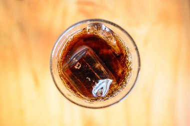 Temiz bardağın tepesinden bakıldığında, içine koyu kahverengi, buzlu bir içecek konur..