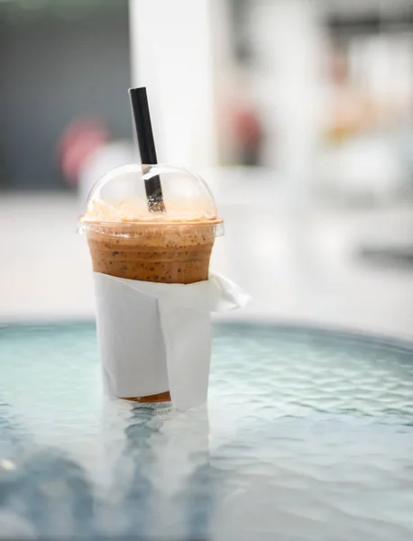 Plastik bardağa yakın çekim, soğuk kahve ile dolu, cam masaya sarılmış beyaz kağıt..