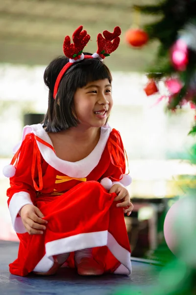 Yıllık Noel partisi için kırmızı elbiseli şirin Asyalı kızın portresi mutlulukla gülümsüyor..