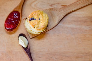 Ahşap bir masada çilek reçeli ve tereyağlı bir çöreğin üst görüntüsü. Bu basit ama klasik bir İngiliz atıştırmalığı..