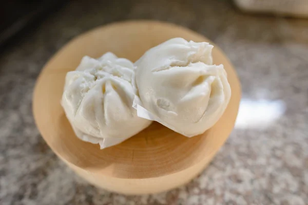 Two steamed buns on a wooden tray. The inside of the bun is hidden in the filling, possibly pork chops, red pork, bamboo shoots, etc.