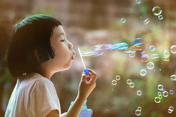 Küçük Asyalı kız sabun köpüğü üflüyor. Eğleniyor ve dışarıda oynamaya konsantre oluyor..