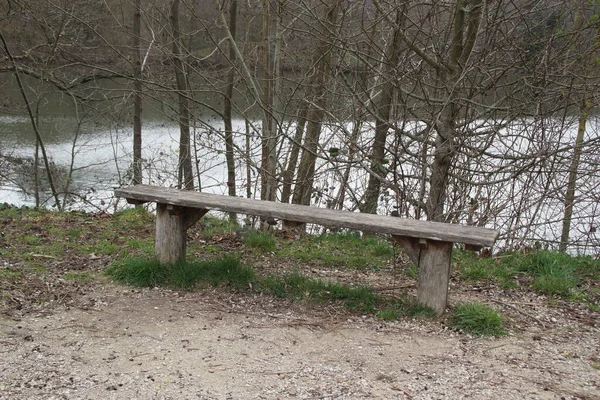 A wooden bench in a forest. Behind the bench there is a pond. It is during the day, there is no one. France, Europe.