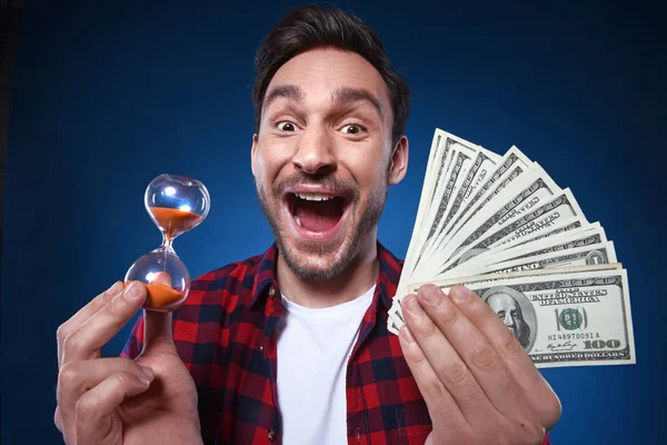 Handsome bearded man in red shirt. Funny guy is a lucky winner, she is holding a pile of money and Hourglass. he is surprised and can\'t believe it, he is happy to win one million dollar jackpot, now he is rich.