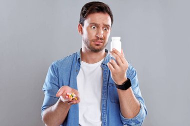 Beyaz bir arka planda bir kutu hap ile izole yakışıklı sakallı adam. Adam bir el hapları tam tutar. Pahalı ilaç hakkında endişeleniyor ama tekrar sağlıklı olmak istiyor.