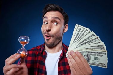 Nakit ve kum saati ile kırmızı tişörtlü yakışıklı sakallı adam. Komik adam a şanslı kazanan, o bir tomar para tutan ve kum saati, bir milyon dolar ikramiye kazanmak mutlu olduğunu, vakit nakittir.