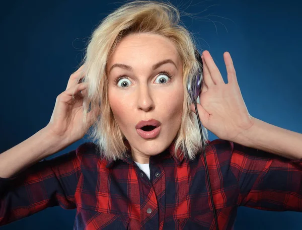 Happy young blonde girl is happy to listen to her favorite music in headphones and sing along to her favorite songs isolated on a blue background