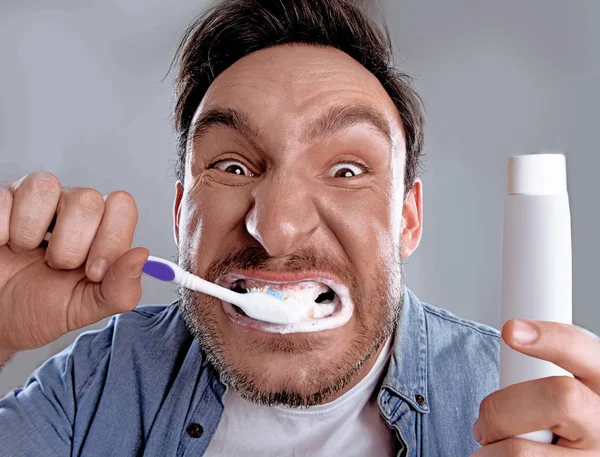 Handsome funny bearded man in whit shirt is obsessed about health of his teeth he cleaned them hard with a toothpaste and a tooth brush and now he is happy