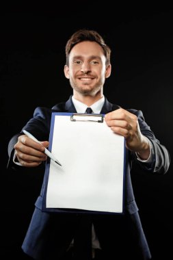 Bir klasik ofis takım elbise ve kravat boş pano siyah bir arka plan üzerinde izole bir sözleşme anlaşma imzalamaya hazır tutmak yakışıklı zeki işadamı