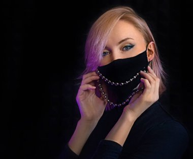 Neon ışıklı kadın Coronavirus 'a karşı cerrahi maske takarak poz veriyor, enfeksiyon kapmış kız covid-19 salgınından korkuyor, maske takıyor, siyah arka planda gizlenmiş hasta var.