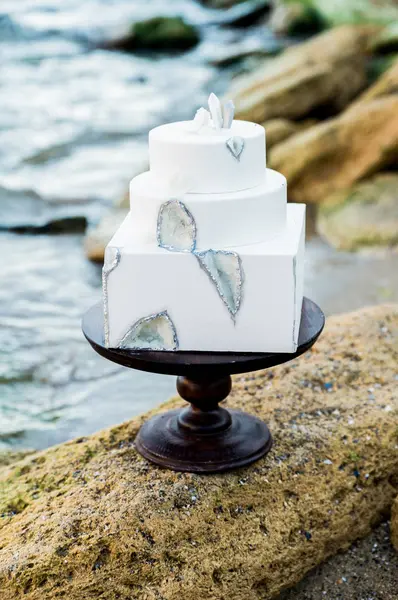 Bir şekilde dekore edilmiş büyük düğün pastası yakın çekim. Deniz tarzı düğün töreni. Deniz sahilinde bir şekilde dekore edilmiş ve şık düğün. Su manzaralı taş kompozisyonu.