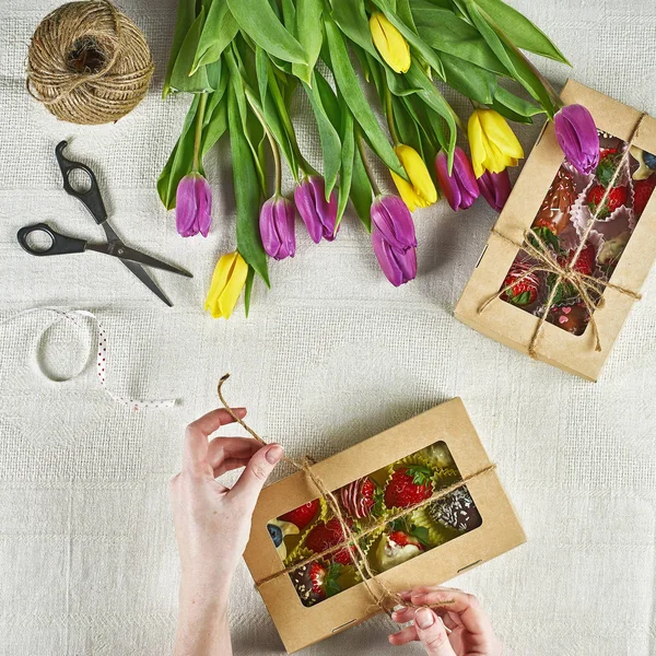 Edible handmade gifts, strawberries in chocolate, macaron, decorated with tulips in a gift box