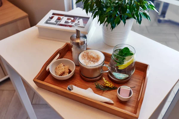 drinks and food on a wooden tray, coffee and lemonade with sweets, a box of tea