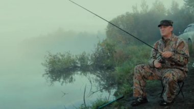 İplik iplik ile bir sisli sabahı göl kıyısında yayılan bir sandalyede oturan balıkçı genel planı ile balıkçı 